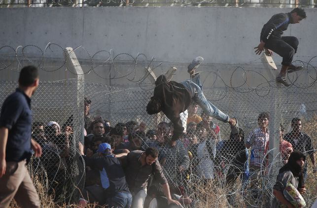 Refugiados sirios cruzan la valla fronteriza que separa su país de Turquía tras romper la alambrada, en la zona de Akcakale. La multitud huye de los enfrentamientos armados en el norte de Siria entre kurdos y los islamistas del autoproclamado Estado Islámico. / (AP Photo/Lefteris Pitarakis).
